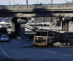 epa09836705 Ukrainian soldiers (top) stand guard on a bridge in front of a damaged Russian army car on the road that leads East of the Ukrainian capital of Kyiv, 19 March 2022. On 24 February Russian troops had entered Ukrainian territory in what the Russian president declared a 'special military operation', resulting in fighting and destruction in the country, a huge flow of refugees, and multiple sanctions against Russia.  EPA/ATEF SAFADI