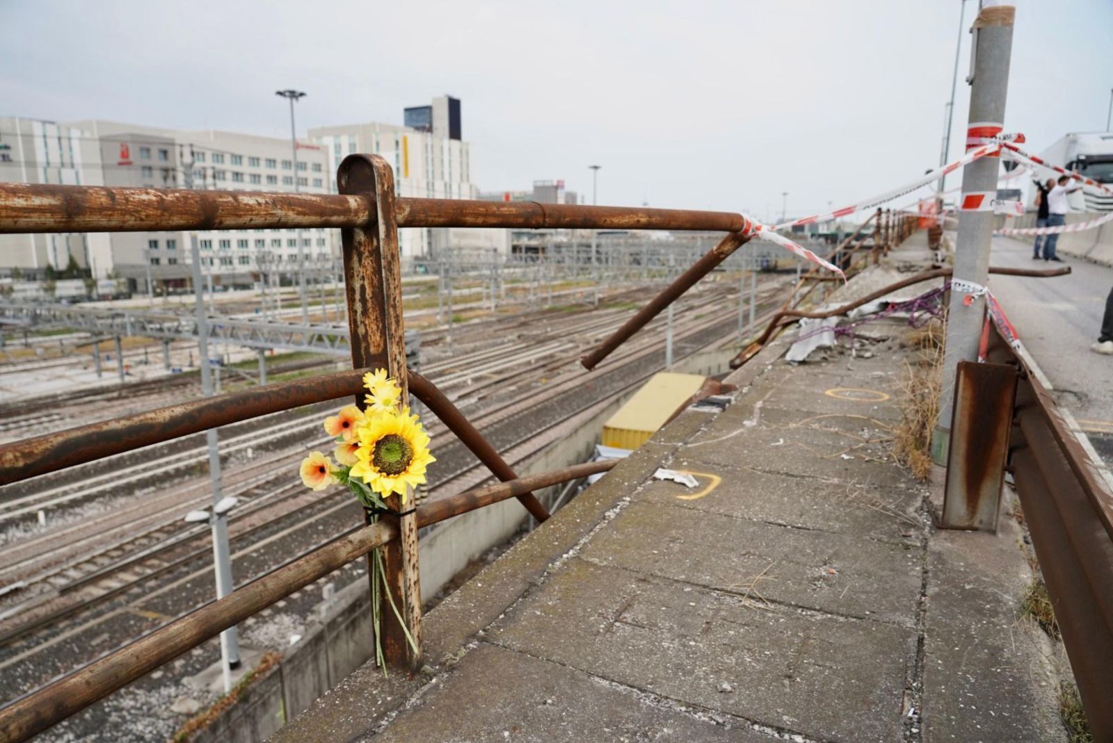 epa10899507 People placed flowers at the site on an overpass from where a bus crashed last night, claiming 21 lives, in Mestre, near Venice, Italy, 04 October 2023. The Venice prefect's department has confirmed that 21 people are dead after a bus plunged from an overpass above a railway line between the districts of Mestre and Marghera on late 03 October. The methane-powered bus burst into flames after falling over 10 meters from the overpass.  EPA/MARCO ALBERTINI