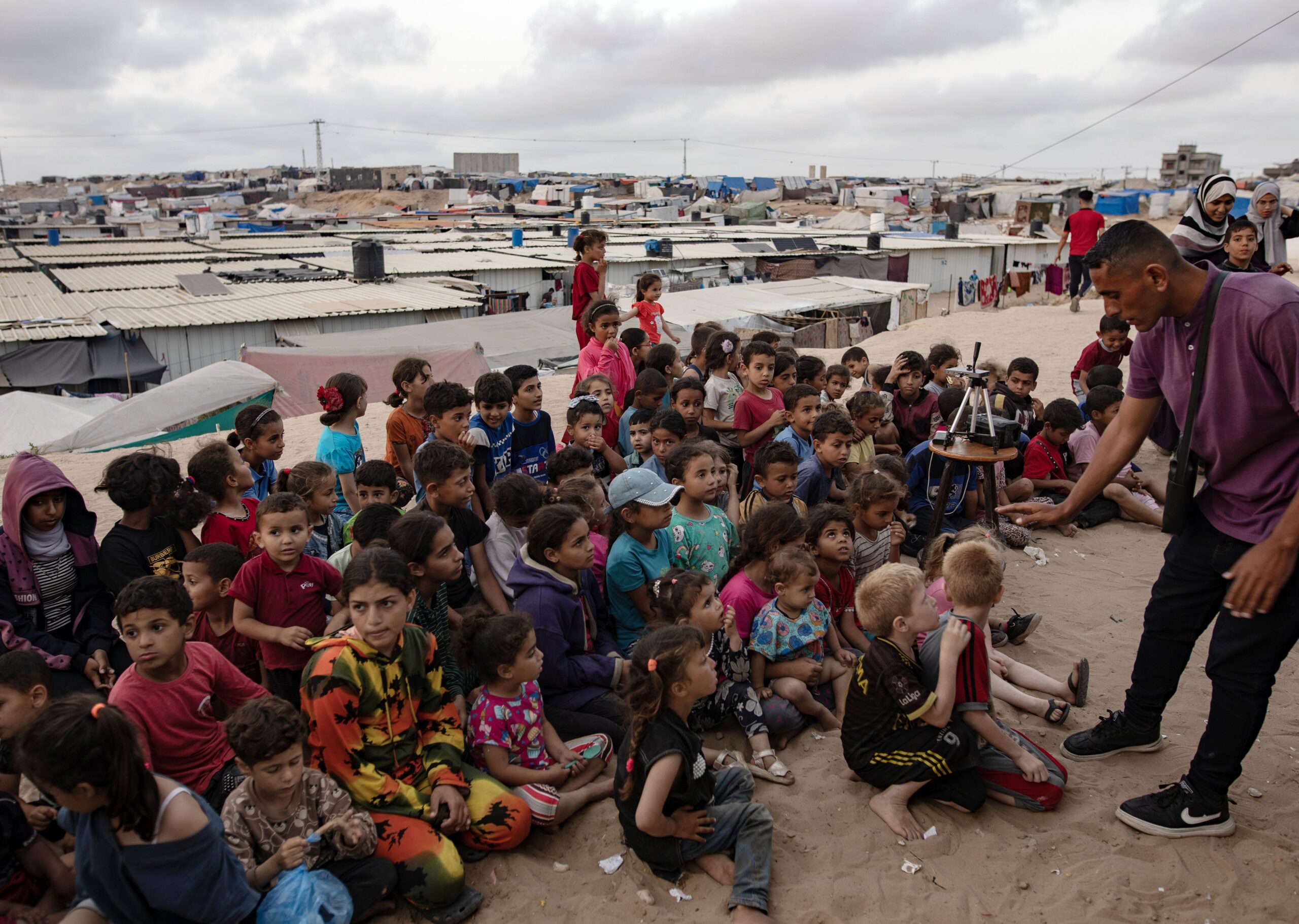 epa11307410 Children gather at a makeshift cinema set up among the tents of the Rafah refugee camp, southern Gaza Strip, 28 April 2024. The cinema was set up by internally displaced Palestinian Muhammad Al-Khudari to entertain children with cartoons. Since 07 October 2023, up to 1.9 million people, or more than 85 percent of the population, have been displaced throughout the Gaza Strip, some more than once, according to the United Nations Relief and Works Agency for Palestine Refugees in the Near East (UNRWA), which added that most civilians in Gaza are in 'desperate need of humanitarian assistance and protection'.  EPA/HAITHAM IMAD