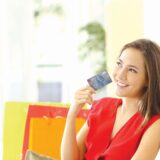 Woman thinking with credit card sitting on a couch with shopping bags at home