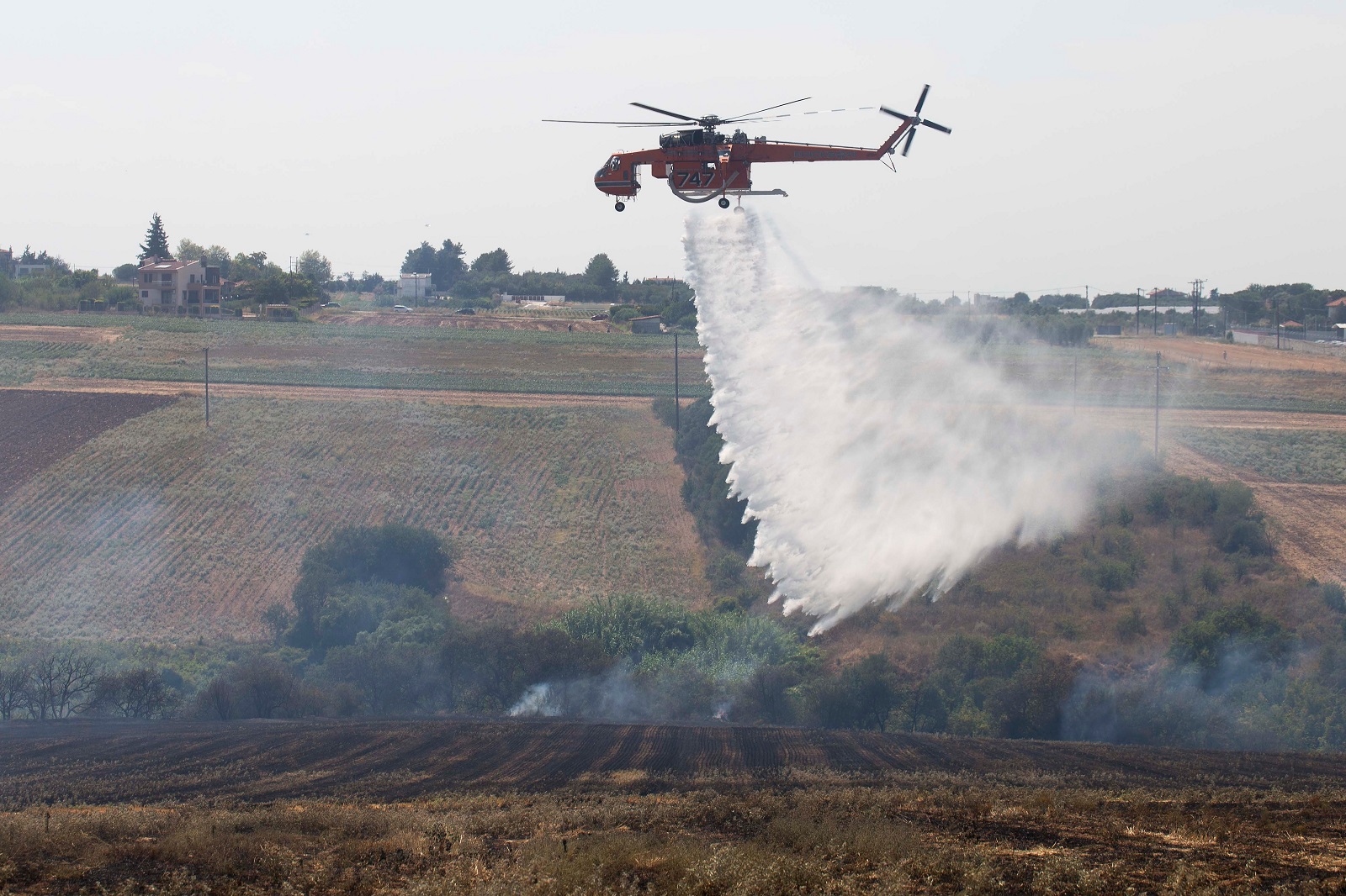 epa11485835 Α firefighting helicopter drops water over a field during a wildfire at Trilofos, near Thessaloniki, Greece, 18 July 2024. A fire that broke out earlier in low vegetation between Trilofos and Plagiario, Thessaloniki, is ongoing. Forty-four firefighters with two groups on foot and 12 fire brigade vehicles are operating to extinguish it. Two of the vehicles and eight firefighters are from Bulgaria, as part of the European Firefighters extension pact. Two firefighting planes and a helicopter are also assisting.  EPA/ACHILLEAS CHIRAS