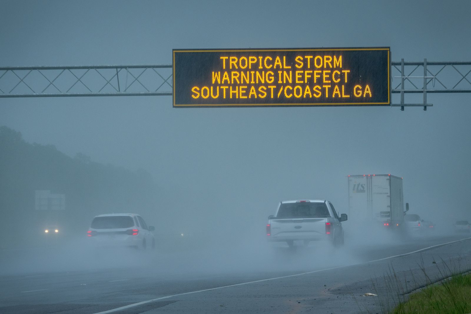 epa11529124 Vehicles pass under a tropical storm warning sign in effect due to tropical storm Debby in Waverly, Georgia, USA, 05 August 2024. Debby made landfall in Florida's Big Bend as a hurricane and is now a tropical storm that can produce potentially historic heavy rainfall across southeast Georgia, part of South Carolina and southeast North Carolina according to the National Hurricane Center.  EPA/CRISTOBAL HERRERA-ULASHKEVICH