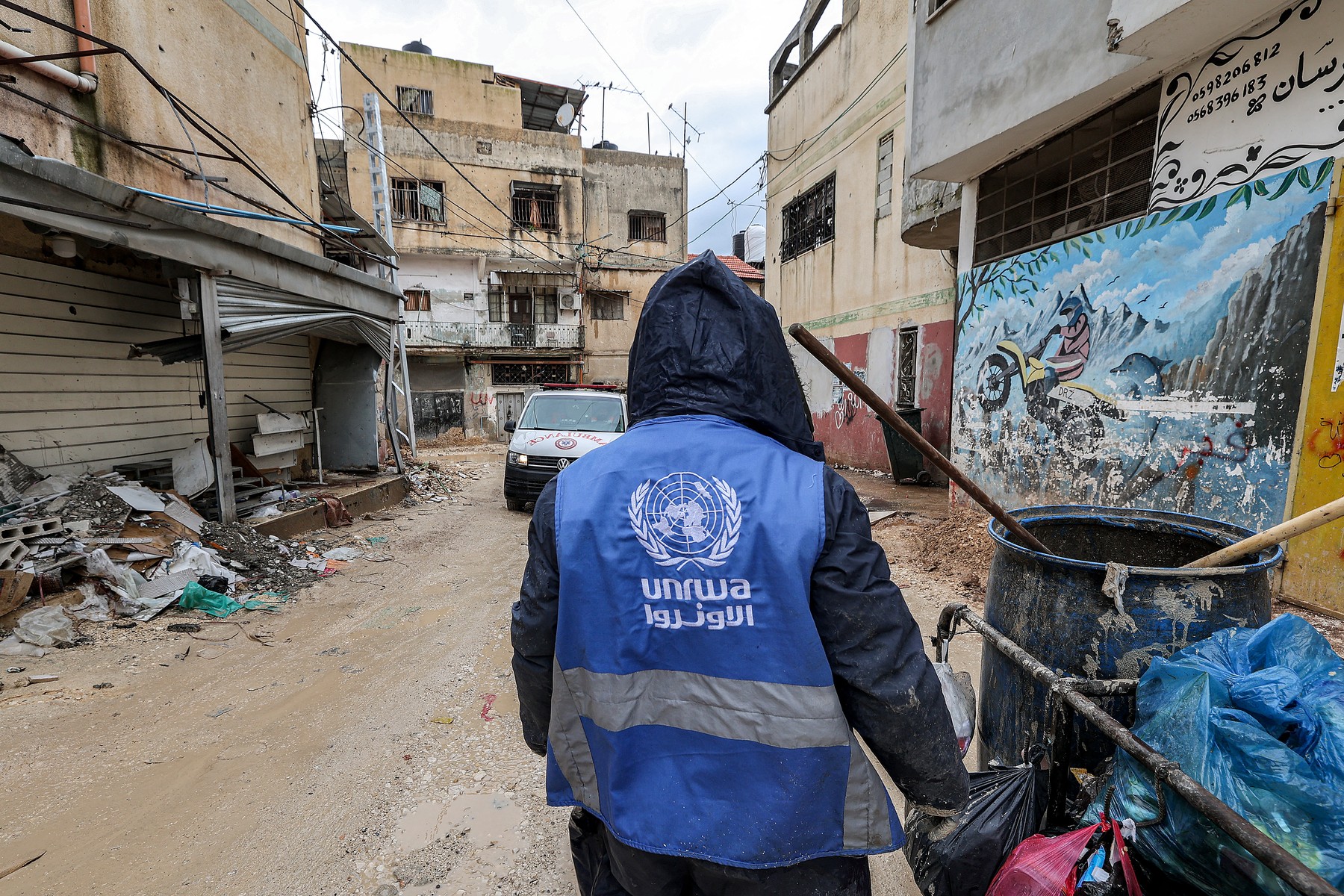 A man collects trash while wearing a jacket bearing the logo of the United Nations Relief and Works Agency for Palestine Refugees in the Near East (UNRWA), along a street in the city of Jenin in the occupied West Bank on January 30, 2024. At least 12 countries -- with top donors the United States and Germany joined by New Zealand on January 30 -- have suspended their funding to UNRWA over Israeli claims that some of its staff members were involved in the October 7 attack.,Image: 841792794, License: Rights-managed, Restrictions: , Model Release: no, Credit line: Jaafar ASHTIYEH / AFP / Profimedia