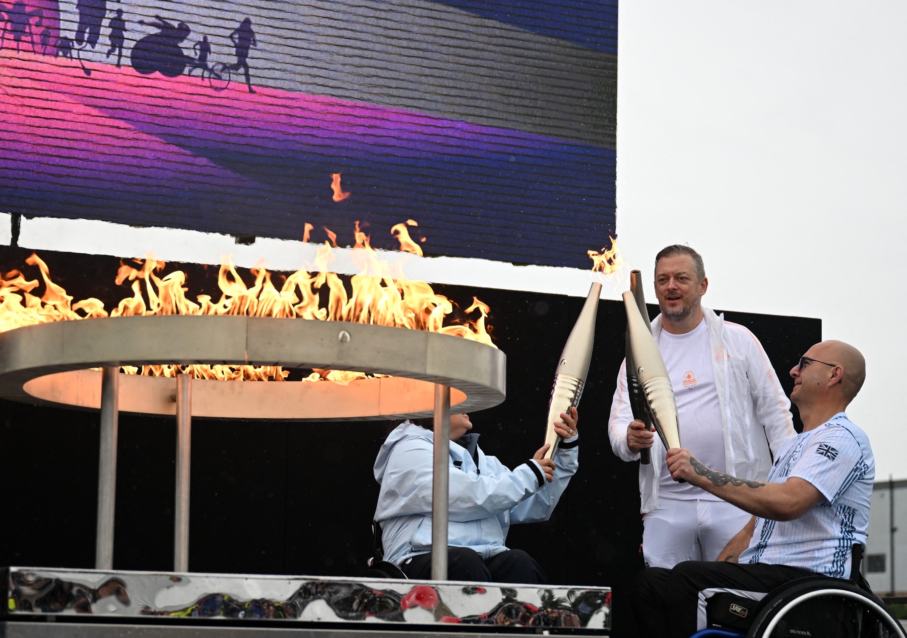 Britain's Helene Raynsford, and Britain's Gregor Ewan, light the torch of President of the International Paralympic Committee Andrew Parsons, lit from the cauldron, during the Paralympic torch-lighting ceremony at Stoke Mandeville in Aylesbury, central England on August 24, 2024. Four days before the Paris Paralympic Games begins, the Paralympic flame was lit on Saturday next to the English hospital where the idea for the competition was born. The Paralympic movement dates back to 1948, when German neurologist Ludwig Guttmann organised sporting events for injured veterans at Stoke Mandeville Hospital, northwest of London. The flame will pass through the Channel Tunnel on Sunday, with 24 British torchbearers taking it halfway, before handing it over to 24 French torchbearers, who will take it to Calais.,Image: 901199721, License: Rights-managed, Restrictions: , Model Release: no, Credit line: JUSTIN TALLIS / AFP / Profimedia