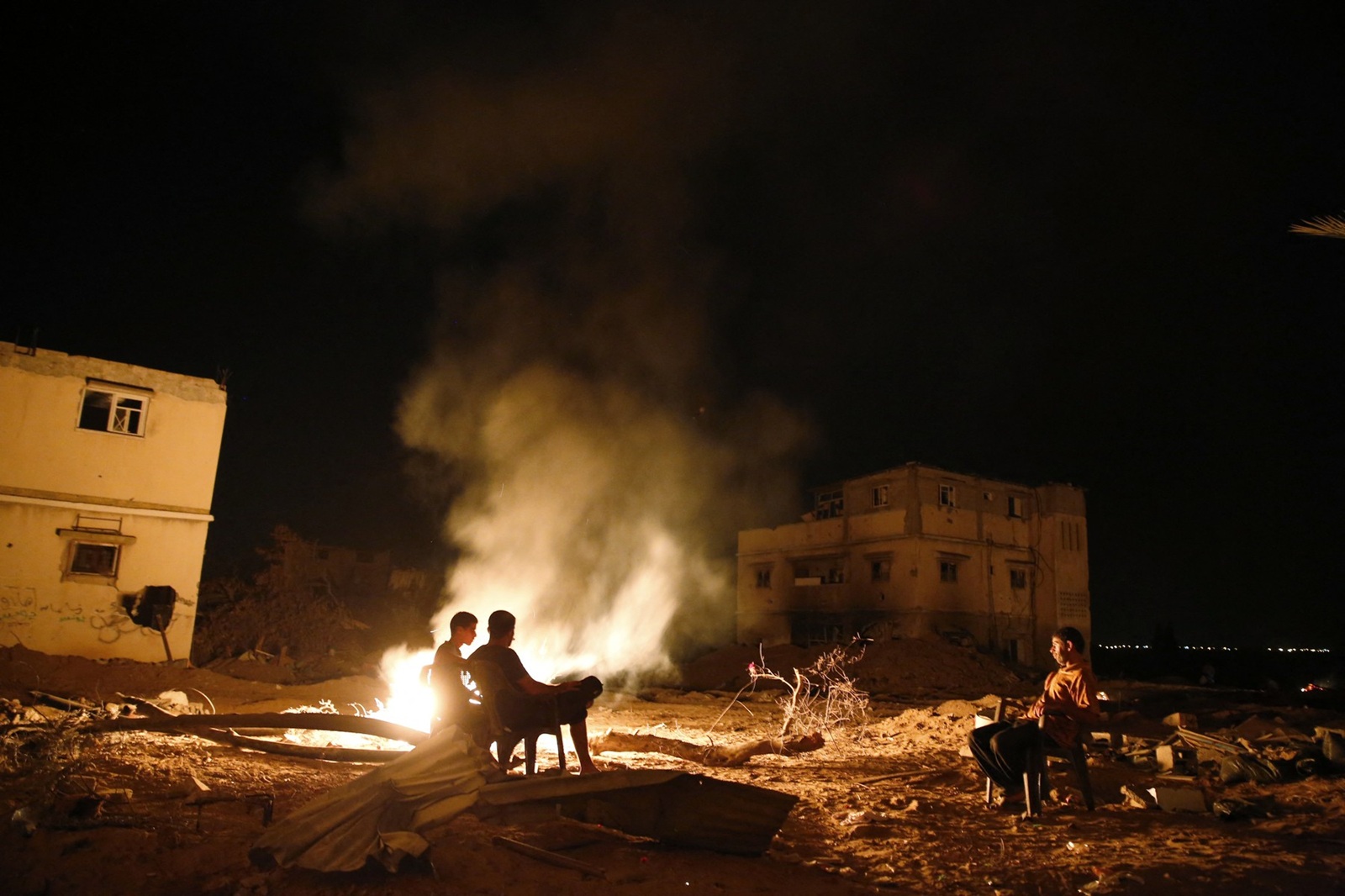 Palestinian men sit next to a fire amid destroyed homes on their block in Shejaiya on August 27, 2014. Shejaiya was one of the hardest hit neighborhoods in fighting between Hamas militants and Israel during 50 days of fighting. The fire was set by the home owners in an effort to keep mosquitoes away from their shattered homes. Israel and Palestinians both boasted of victory in the Gaza war but analysts say Hamas received only promises while the conflict aggravated divisions in the Israeli leadership.,Image: 203136918, License: Rights-managed, Restrictions: , Model Release: no, Credit line: ROBERTO SCHMIDT / AFP / Profimedia