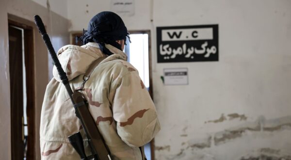 epa11754246 A member of the Syrian opposition stands next to a sign with Persian inscription reading 'Death to America' at a military position allegedly used by Iranian forces after it was captured by the Syrian opposition in the city of Khan Sheikhoun, Idlib countryside, Syria, 03 December 2024. Syrian opposition forces, led by the Islamist militant group Hayat Tahrir al-Sham (HTS), launched an offensive on 27 November, taking large parts of Aleppo, Syria's second-largest city. The offensive triggered counterattacks by the Syrian regime forces as well as Russian and Syrian airstrikes on opposition-controlled areas.  EPA/MOHAMMED AL RIFAI