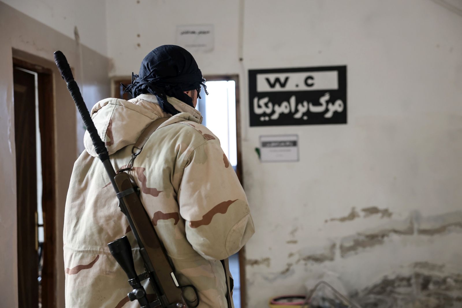 epa11754246 A member of the Syrian opposition stands next to a sign with Persian inscription reading 'Death to America' at a military position allegedly used by Iranian forces after it was captured by the Syrian opposition in the city of Khan Sheikhoun, Idlib countryside, Syria, 03 December 2024. Syrian opposition forces, led by the Islamist militant group Hayat Tahrir al-Sham (HTS), launched an offensive on 27 November, taking large parts of Aleppo, Syria's second-largest city. The offensive triggered counterattacks by the Syrian regime forces as well as Russian and Syrian airstrikes on opposition-controlled areas.  EPA/MOHAMMED AL RIFAI