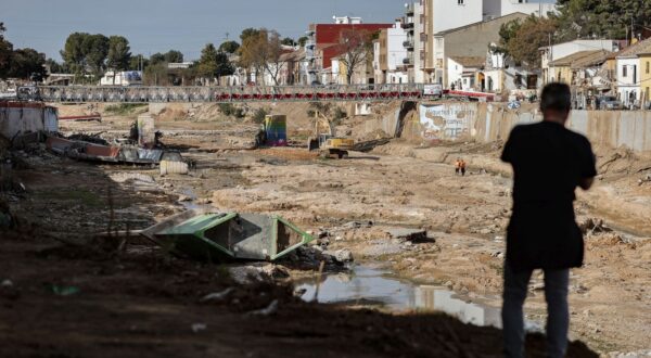 epa11760662 A man watches an excavator that is working on the bed of the Poyo ravine as it passes through Picanya, Valencia, Spain, 06 December 2024.  EPA/MANUEL BRUQUE