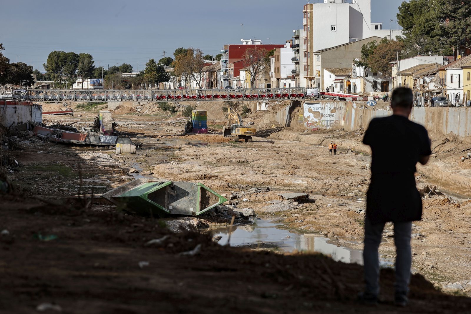 epa11760662 A man watches an excavator that is working on the bed of the Poyo ravine as it passes through Picanya, Valencia, Spain, 06 December 2024.  EPA/MANUEL BRUQUE