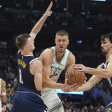 Boston Celtics center Kristaps Porzingis, center, drives to the basket as Denver Nuggets guard Christian Braun, left, and forward Dario Saric defend in the first half of an NBA basketball game, Tuesday, Jan. 7, 2025, in Denver. (AP Photo/David Zalubowski)