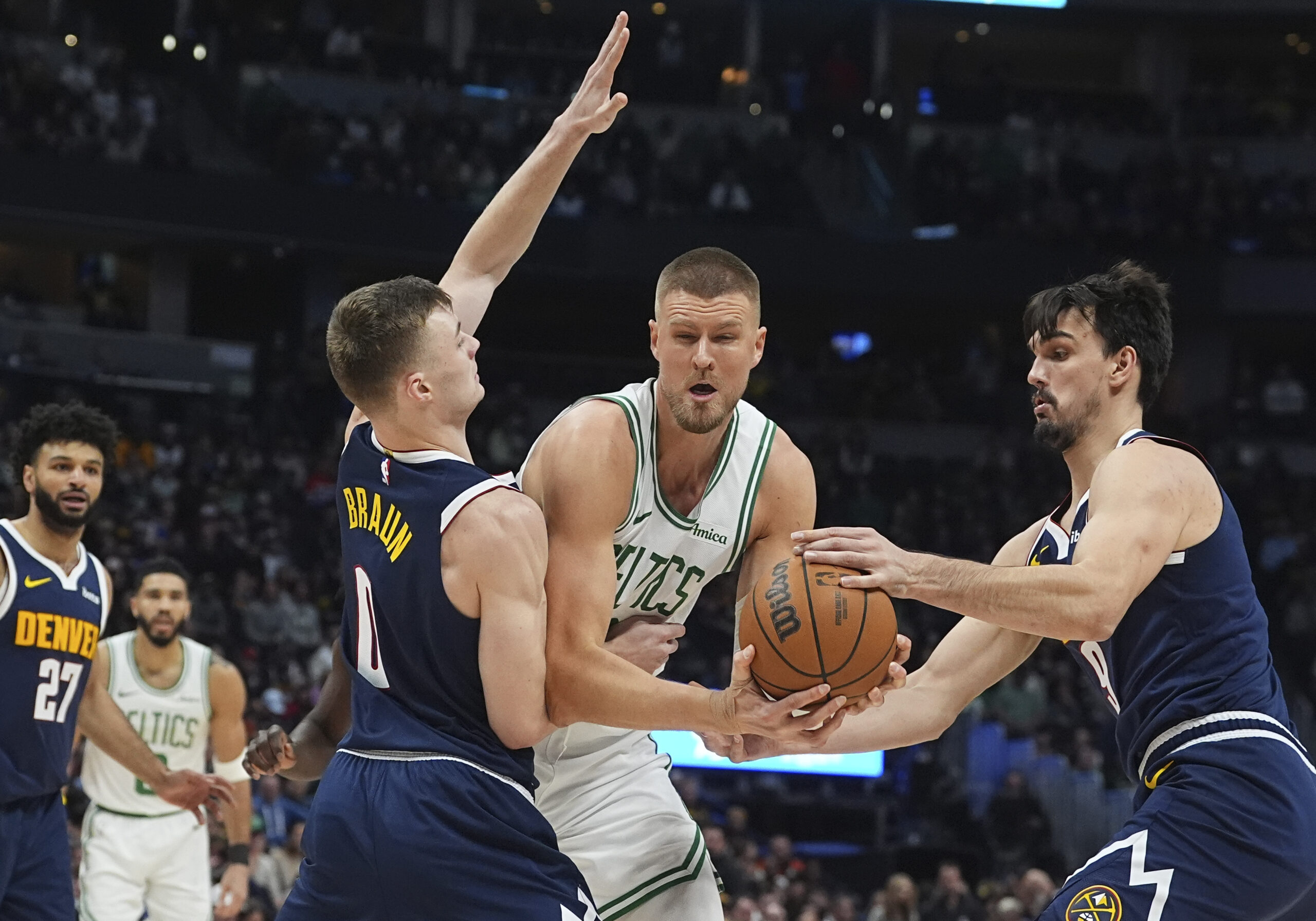 Boston Celtics center Kristaps Porzingis, center, drives to the basket as Denver Nuggets guard Christian Braun, left, and forward Dario Saric defend in the first half of an NBA basketball game, Tuesday, Jan. 7, 2025, in Denver. (AP Photo/David Zalubowski)