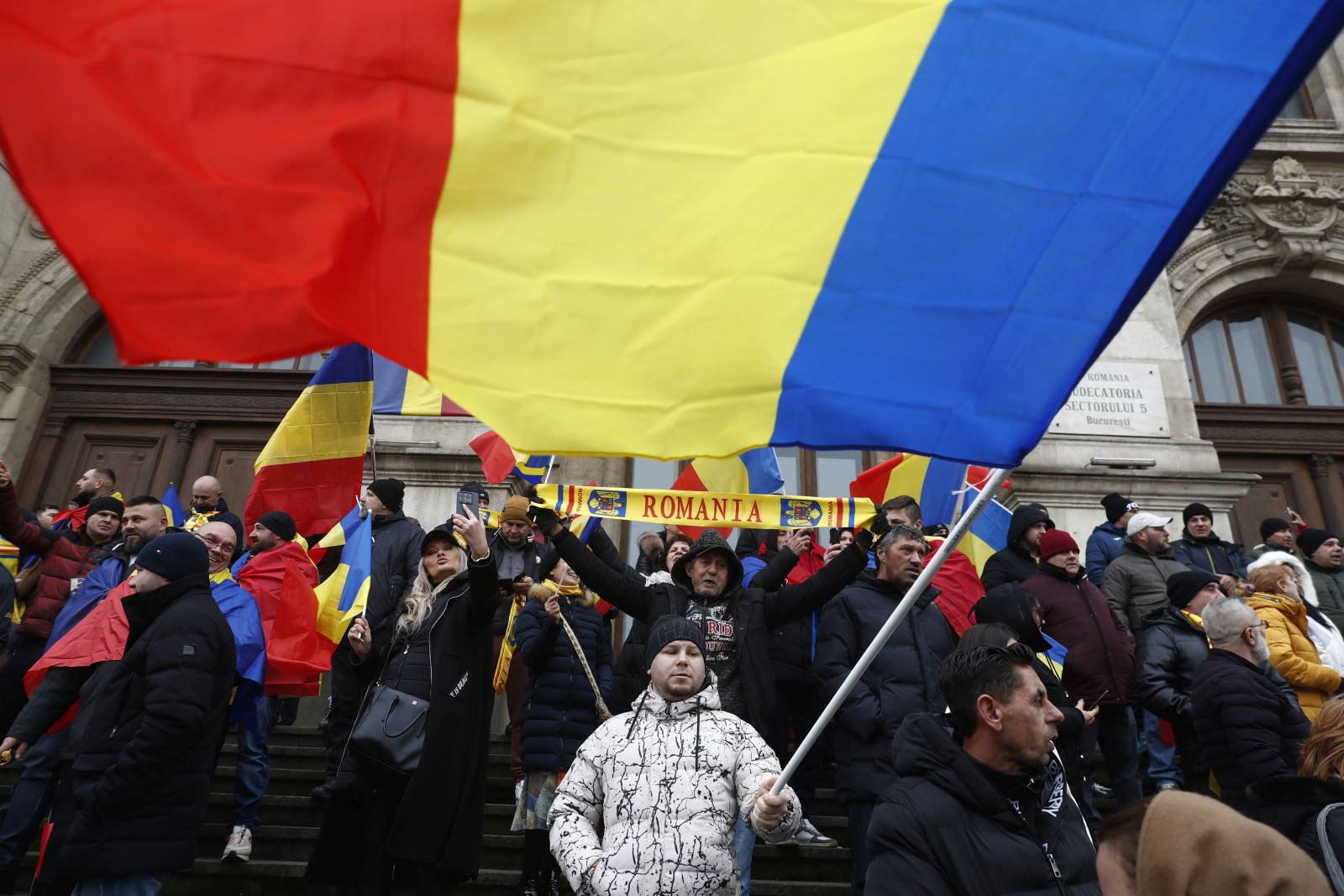 epa11799300 Supporters of independent candidate Calin Georgescu (not pictured) wave Romanian national flags as they gather on the steps of the Bucharest Court of Appeal headquarters in Bucharest, Romania, 30 December 2024. Georgescu, winner of the first round of the annulled presidential elections, filed a lawsuit challenging the Central Electoral Bureau's annulment of the entire electoral process and the resumption of the presidential elections, based on the Romanian Constitutional Court's ruling, and pressed charges against several prominent political figures and institutions in Romania.  EPA/BOGDAN CRISTEL