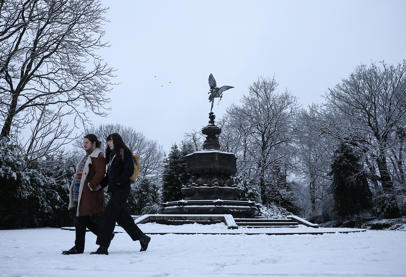 epa11806789 People walk in the snow near the Statue of Eros at Sefton Park in Liverpool, Britain, 05 January 2025. The Met Office has issued a yellow warning for snow and ice across nearly all of Britain, with a more severe amber snow warning in place throughout much of northern Britain and Wales.  EPA/ADAM VAUGHAN