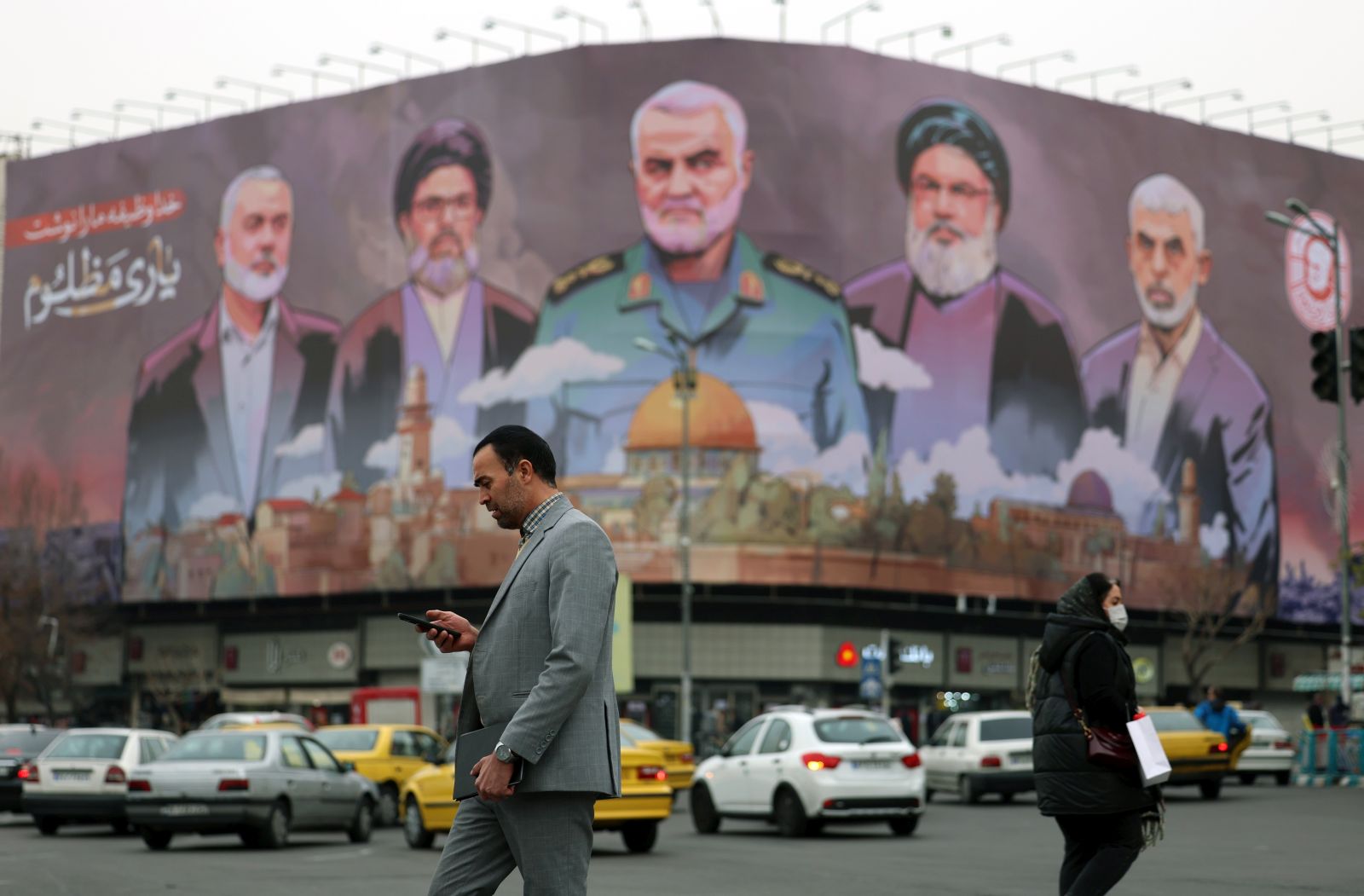 epa11808827 Iranians walk past a billboard with the pictures of late Iranian Islamic Revolutionary Guard Corps (IRGC) Quds Force commander Qasem Soleimani (C), late Hamas leaders Ismail Haniyeh (L) and Yahya Sinwar (R), and late Hezbollah leader Hasan Nasrallah (2-R), and the head of Hezbollah's executive council Hashem Safieddine (2-L), and a sentence reading in Persian 'God wrote our duty, help to the oppressed' hanging at the Enghelab square in Tehran, Iran, 06 January 2025.  EPA/ABEDIN TAHERKENAREH