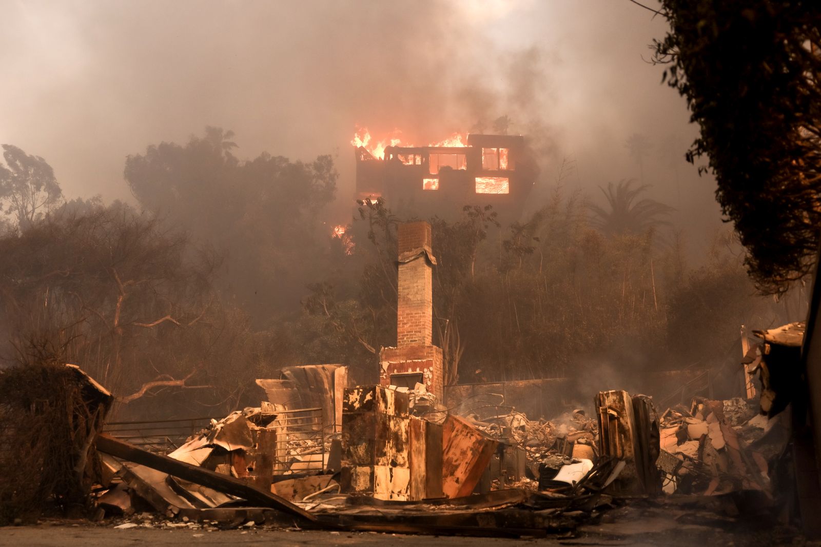 epa11813471 A house on fire and the remains of another burnt home in an area affected by the Palisades wildfire in Malibu, California, USA, 08 January 2025. According to data from California Department of Forestry and Fire Protection, CAL FIRE, the Palisades fire has burned through thousands of acres and has forced tens of thousands of evacuations in the Los Angeles area.  EPA/ALLISON DINNER