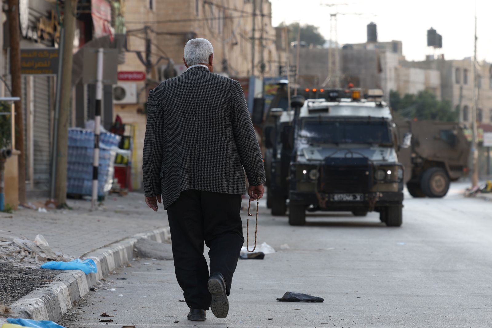 epa11816836  Palestinian man walks pass Israeli troops during army operation at Qabaitya village near the West Bank city of Jenin, 10 January 2025. Several Palestinians were wounded during the operation, according to the Palestinian Health Ministry.  EPA/ALAA BADARNEH