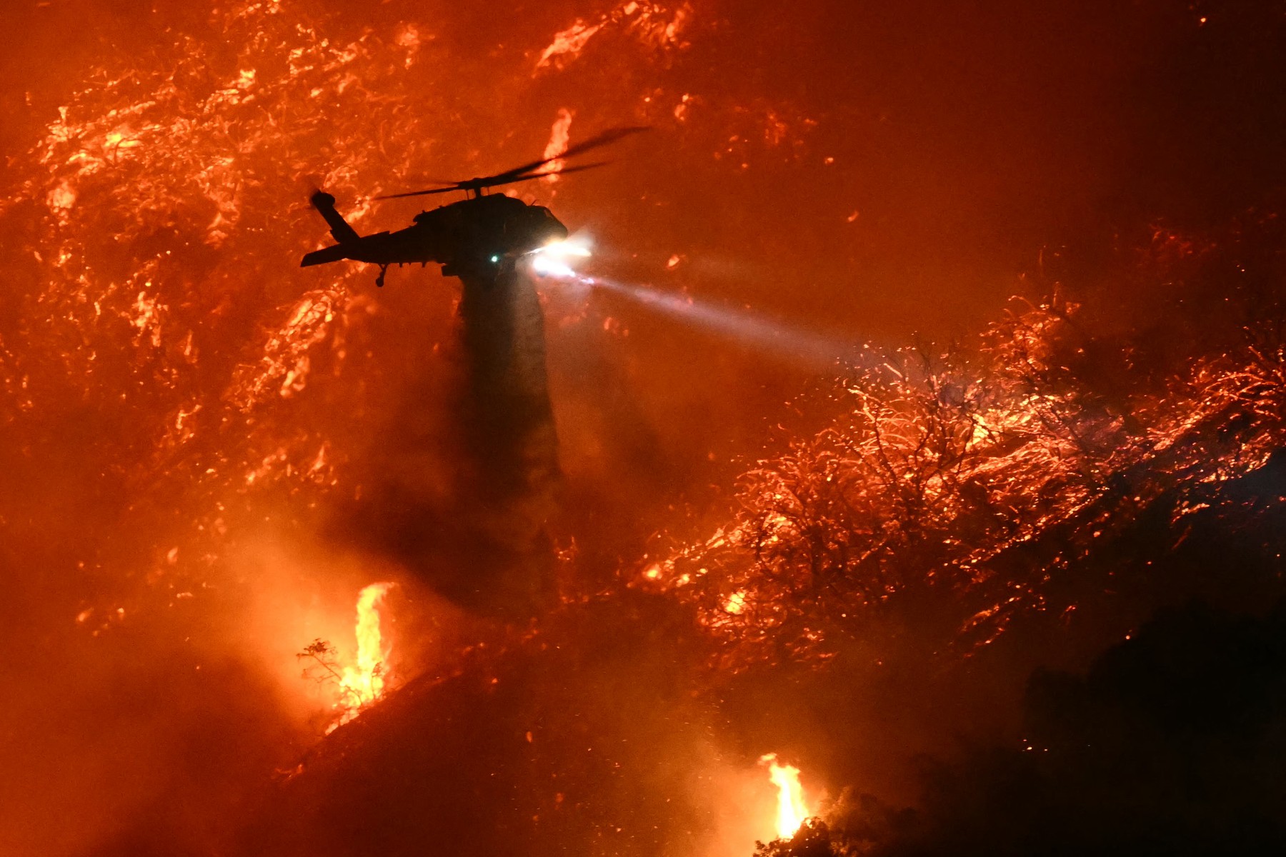 A fire fighting helicopter drops water as the Palisades fire grows near the Mandeville Canyon neighborhood and Encino, California, on January 11, 2025. The Palisades Fire, the largest of the Los Angeles fires, spread toward previously untouched neighborhoods January 11, forcing new evacuations and dimming hopes that the disaster was coming under control. Across the city, at least 11 people have died as multiple fires have ripped through residential areas since January 7, razing thousands of homes in destruction that US President Joe Biden likened to a "war scene.",Image: 953064912, License: Rights-managed, Restrictions: , Model Release: no, Credit line: Patrick T. Fallon / AFP / Profimedia