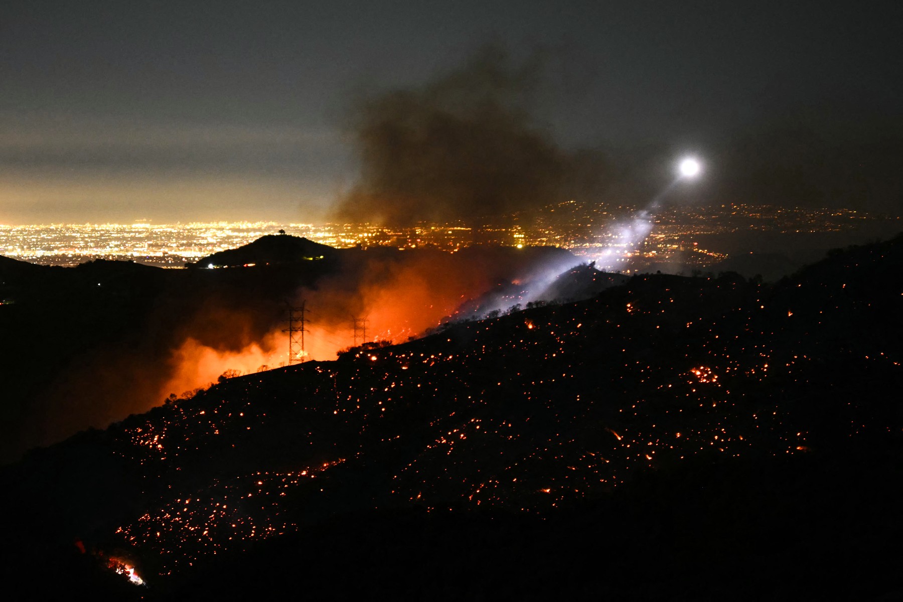 The light of a fire fighting helicopter illuminates a smouldering hillside as the Palisades fire grows near the Mandeville Canyon neighborhood and Encino, California, on January 11, 2025. The Palisades Fire, the largest of the Los Angeles fires, spread toward previously untouched neighborhoods January 11, forcing new evacuations and dimming hopes that the disaster was coming under control. Across the city, at least 11 people have died as multiple fires have ripped through residential areas since January 7, razing thousands of homes in destruction that US President Joe Biden likened to a "war scene.",Image: 953067535, License: Rights-managed, Restrictions: , Model Release: no, Credit line: Patrick T. Fallon / AFP / Profimedia